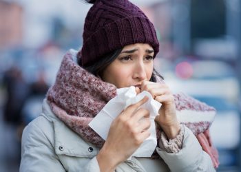 Young woman coughing during winter on street. Girl with cold wearing knitted cap and scarf feeling unwell. Woman feeling sick during for winter and city pollution. Girl with sore throat.